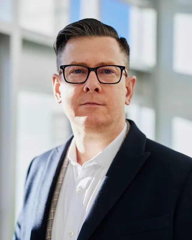 Portrait of a man wearing glasses and a dark blazer.
